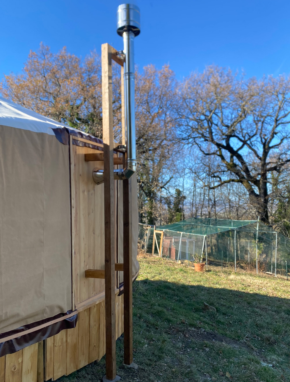 Vista posteriore di una yurta con canna fumaria esterna in metallo, sostenuta da una struttura in legno